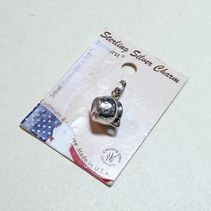 May include: A sterling silver charm shaped like a small teapot, attached to a white display card. The card features the text Sterling Silver Charm, Sunburst, and Made in U.S.A. along with a small American flag graphic and a circular logo.
