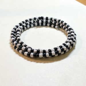 May include: A spiral bracelet composed of alternating black and white beads. The bracelet is coiled, creating a layered effect. The beads are small and evenly spaced, giving the bracelet a textured appearance. The color scheme is simple and classic.