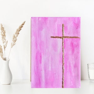 May include: A pink canvas painting with a gold cross in the center. The cross is made of a thin, textured line.