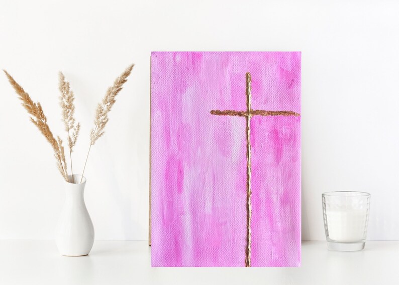 May include: A pink canvas painting with a gold cross in the center. The cross is made of a thin, textured line.