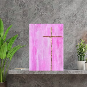 May include: A pink canvas painting with a gold cross in the center. The cross is made of thin, gold twine.