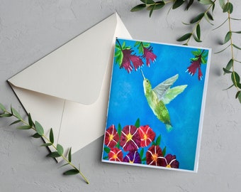 May include: A greeting card featuring a green hummingbird in flight, with its beak extended towards a cluster of red flowers. The hummingbird is against a bright blue background, with more red flowers at the bottom of the card.