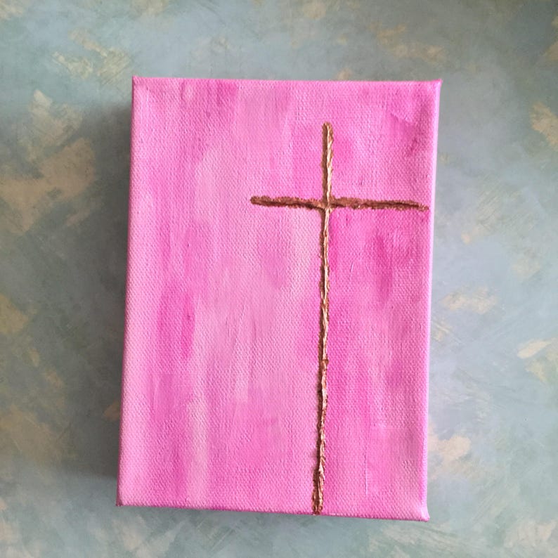 May include: A pink canvas painting with a gold cross painted on it.