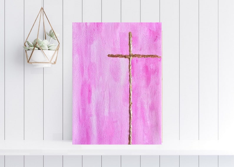 May include: A pink canvas painting with a gold cross in the center. The cross is painted with a textured, brushstroke effect.