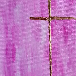 May include: A gold cross painted on a pink canvas background. The cross is thin and has a slightly textured appearance.