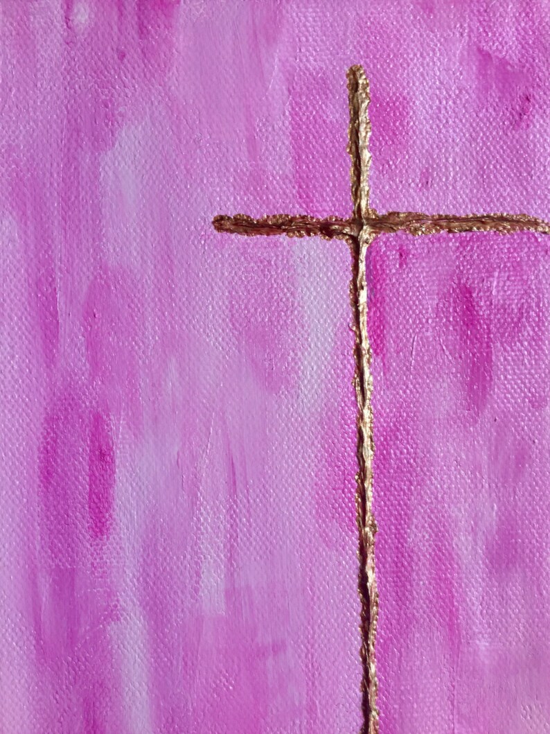 May include: A gold cross painted on a pink canvas background. The cross is thin and has a slightly textured appearance.