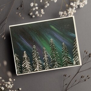 May include: A painting of a snowy forest with a green and purple aurora borealis in the night sky.