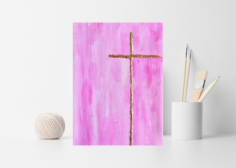 May include: A simple gold cross painted on a pink background. The cross is painted with a textured brushstroke.