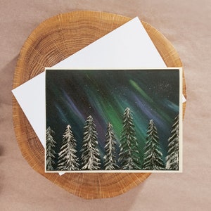 May include: A painting of a snowy forest with a vibrant green, blue, and purple aurora borealis in the night sky.