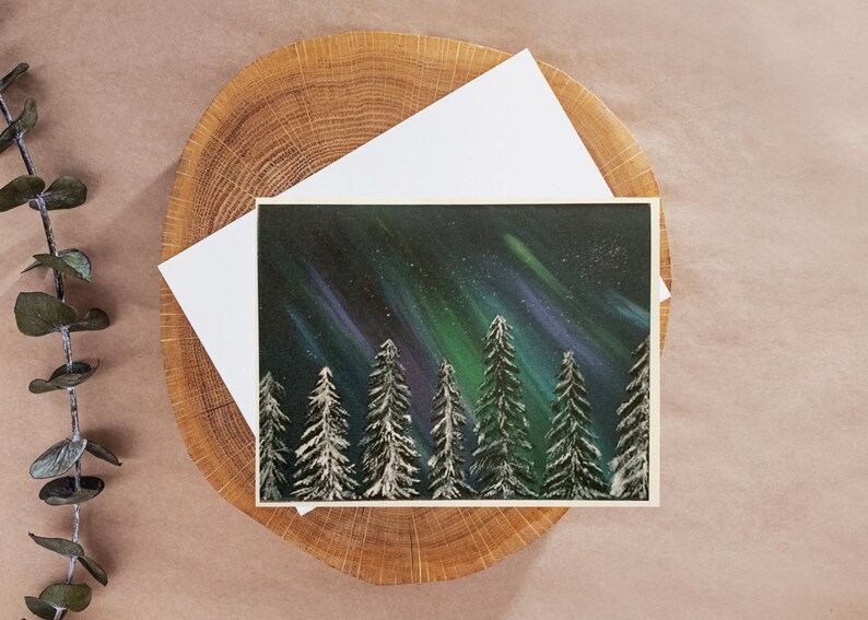 May include: A painting of a snowy forest with a vibrant green, blue, and purple aurora borealis in the night sky.