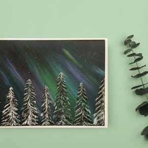 May include: A painting of a snowy forest with a vibrant green, purple, and blue aurora borealis in the night sky.