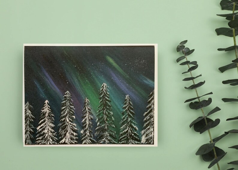 May include: A painting of a snowy forest with a vibrant green, purple, and blue aurora borealis in the night sky.