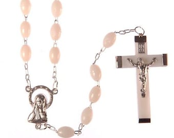 May include: A white rosary with oval-shaped beads and a silver crucifix with a figure of Jesus Christ. The crucifix has the inscription "IN RI" on the back.