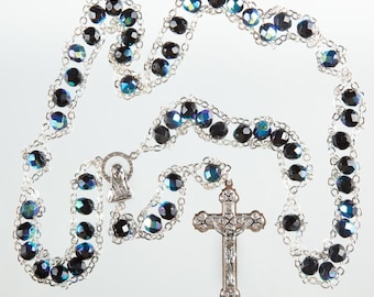 May include: A silver rosary with black and blue iridescent beads and a silver crucifix.