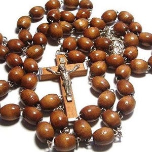 Może przedstawiać: Różaniec z brązowego drewna z drewnianym krucyfiksem z srebrną figurką Jezusa. Korale różańca są owalne.