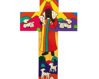 May include: A colorful wooden cross with a depiction of Jesus carrying a lamb. The cross is painted with a rainbow of colors and features a sun in the top section. The background is a purple, pink, and green landscape with white sheep.