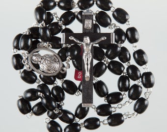 May include: A black wooden rosary with a silver crucifix and a silver medal featuring a depiction of the Sacred Heart of Jesus. The rosary beads are oval-shaped and the crucifix has a dark wood finish.