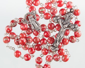May include: A red rosary with a silver crucifix and a silver charm of the Virgin Mary. The beads are made of red stone with white speckles.