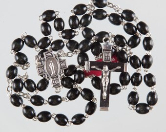 May include: A black wooden rosary with a silver crucifix and a silver medal of the Virgin Mary. The rosary beads are oval shaped.