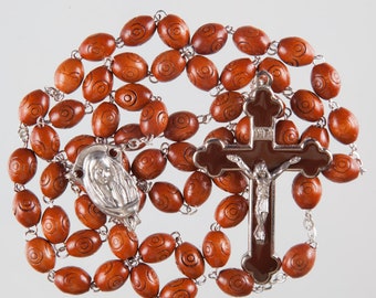 May include: A brown wooden rosary with a silver crucifix and a silver pendant featuring the Virgin Mary. The beads are oval-shaped and have a swirl pattern.