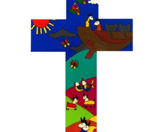 May include: A wooden cross painted with a colorful scene of animals, birds, and butterflies. The top of the cross features a blue sky with a sun, clouds, and three birds flying. The middle section shows a boat with three animals inside, and the bottom section shows a green field with animals and butterflies.