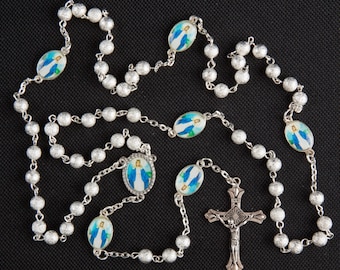 May include: A silver rosary with blue and white oval beads featuring an image of the Virgin Mary. The rosary has a silver crucifix with a white image of Jesus.