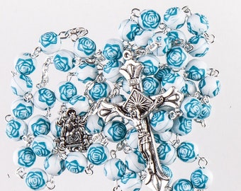 May include: White and blue rosary beads with a silver crucifix and a silver charm of the Virgin Mary and baby Jesus. The beads are decorated with blue roses.