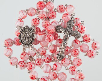 May include: A pink and white rosary with a silver crucifix and a silver medal of the Virgin Mary. The beads are made of glass and have a floral pattern.