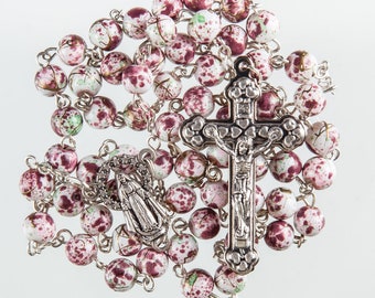 May include: A rosary with speckled beads in white, pink, and green hues. The silver-toned crucifix and centerpiece feature detailed religious figures. The beads are strung together, forming a complete loop.