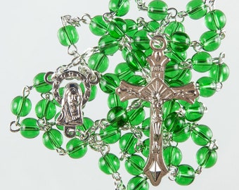 May include: A green glass rosary with a silver crucifix and a silver charm featuring a depiction of the Virgin Mary.