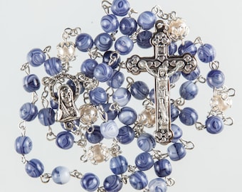 May include: A blue and white rosary with a silver crucifix and a silver charm of the Virgin Mary. The beads are made of a blue and white marbled material.