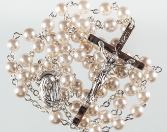 May include: A white pearl rosary with a silver crucifix and a silver pendant featuring a depiction of the Virgin Mary.
