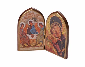 May include: A wooden diptych icon with two panels. The left panel depicts the Holy Trinity, three figures seated at a table with a chalice. The right panel depicts the Virgin Mary holding the baby Jesus. Both panels have a gold background and are framed in brown wood.