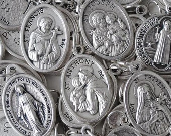 May include: A collection of silver-toned metal medallions featuring various Catholic saints. Each medallion has a raised image of a saint and includes the saint's name and the word "Italy".