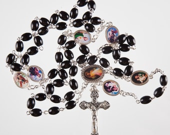 May include: A black rosary with oval beads and silver-toned chain links. The rosary features several oval medallions with religious imagery and a detailed crucifix pendant at the bottom. The beads are dark and glossy.