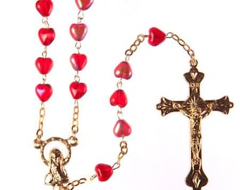 May include: A gold rosary with red heart-shaped beads and a gold crucifix.