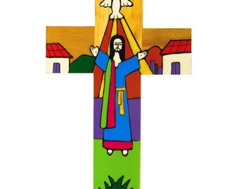 May include: A wooden cross with a colorful painted design depicting Jesus Christ with outstretched arms, a dove above him, and a rainbow. The background includes green grass, a blue sky, and two houses with red roofs.