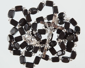 May include: A black wooden rosary with a silver crucifix and a silver pendant featuring a depiction of the Virgin Mary and baby Jesus.