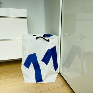 May include: White laundry bag with blue number "11" printed on the front. The bag has a drawstring closure and black handles.