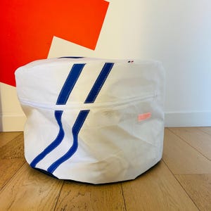 May include: White canvas storage bag with blue stripes and a zipper closure. The bag has a small pink label with text.