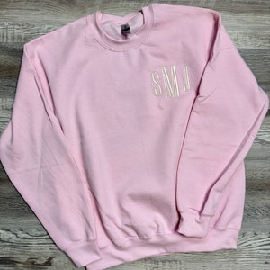 May include: A pink sweatshirt with the letters "SMJ" embroidered on the front in white.
