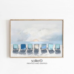 May include: A framed print featuring a beach scene with seven blue and teal beach chairs lined up on the sand. The background shows a light blue sky, ocean, and a setting sun. The print has a wooden frame.