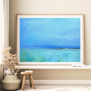 May include: Abstract painting of a seascape with a blue sky and turquoise water. The painting is framed in a light wood frame and is hanging on a wall.