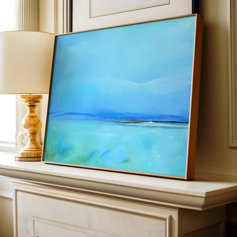 May include: A framed abstract painting of a seascape with a blue sky and turquoise water. The painting is in a gold frame and is hanging on a white wall.