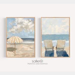 May include: Two framed paintings depicting a beach scene. The left painting shows a striped beach umbrella on a sandy beach with blue sky and clouds. The right painting shows two beach chairs facing the ocean with blue water and white clouds.
