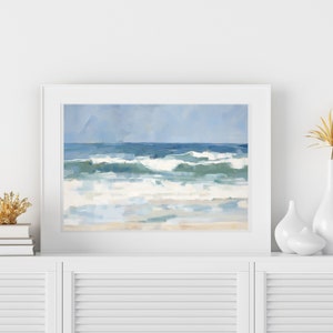 May include: A framed painting of a seascape with blue and white waves crashing on a sandy beach. The sky is a light blue with a few clouds.