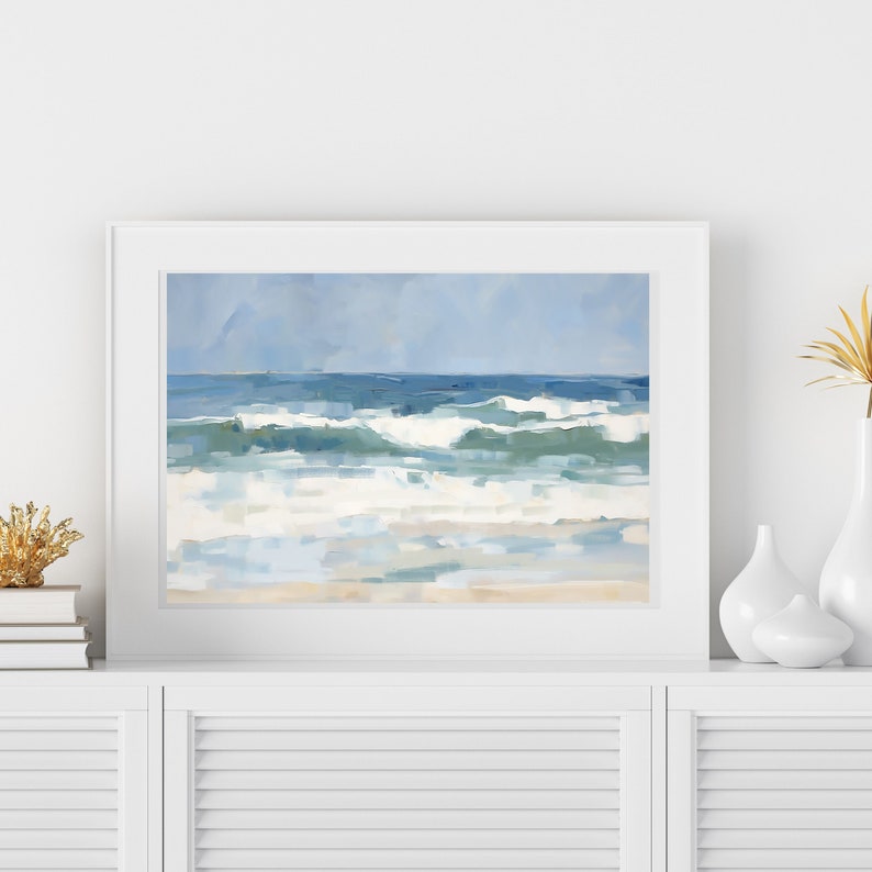 May include: A framed painting of a seascape with blue and white waves crashing on a sandy beach. The sky is a light blue with a few clouds.