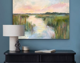 May include: An abstract landscape painting depicts a marsh scene with a waterway reflecting the sky. The artwork features a palette of greens, blues, pinks, and yellows. The painting hangs above a black console table with a lamp, figurine, and a book.