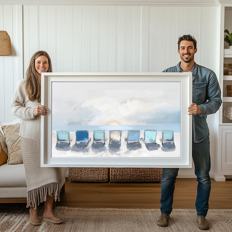 May include: A framed art print depicting six beach chairs on a sandy shore under a cloudy sky. The chairs are various shades of blue and turquoise. The artwork is held by a man and a woman.