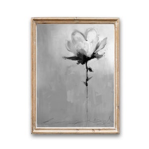 A framed grayscale painting of a single flower. The flower is rendered in a loose, expressive style with shades of gray and white. The background is a textured gray canvas. The painting is in a light beige wooden frame.  The artist's signature is visible at the bottom. The overall style is modern and abstract.